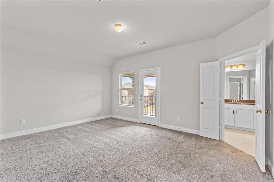 Unfurnished bedroom featuring lofted ceiling, access to exterior, ensuite bath, and light carpet