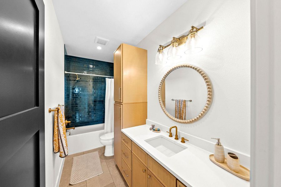 Elegant gold hardware accents a light wood vanity paired with a deep blue tiled shower.