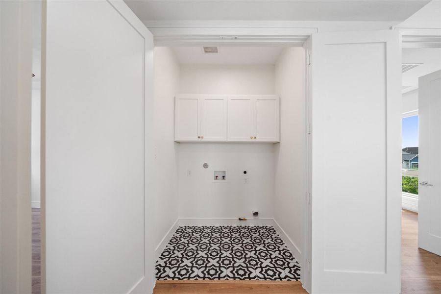 Laundry area with white cabinets, patterned floor tiles, and space for a washer and dryer.