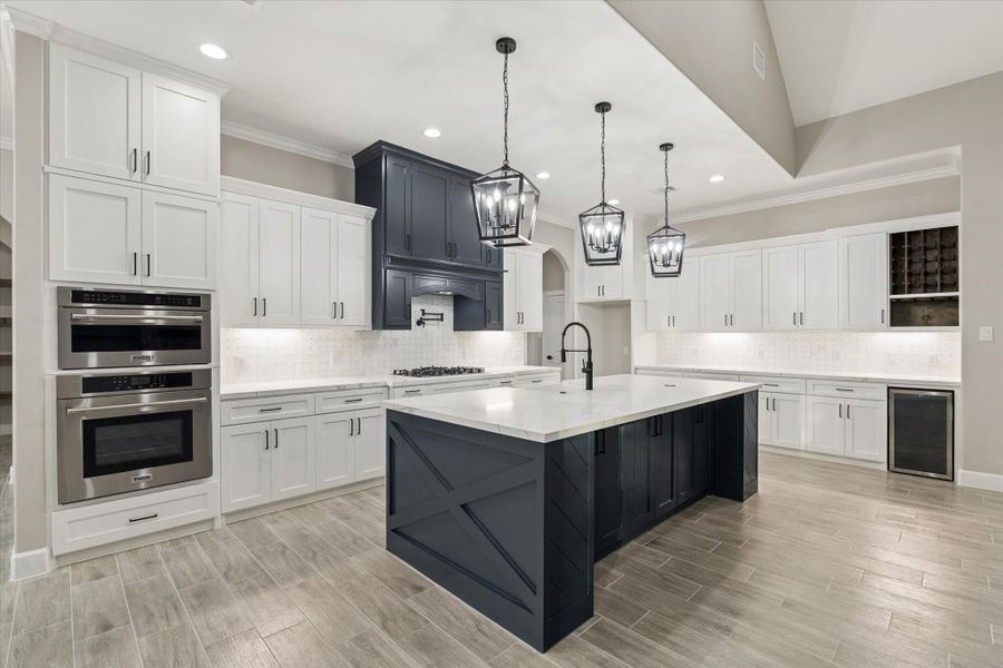 View of large kitchen with island breakfast bar and under storage.  Three pendant lights and quartz counters.  Built in wine storage and wine fridge.  30" Thor wall oven and 1.6 cu ft Thor microwave.  36 inch Thor gas cooktop 6 burners. Pot filler.  Custom pull out cabinets.  Under-cabinet lighting.