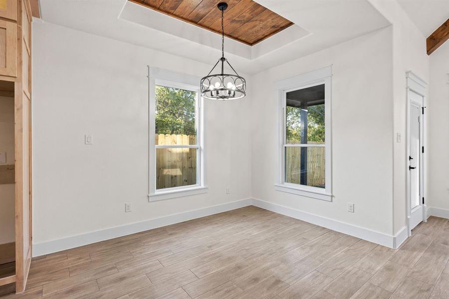 Unfurnished dining area with a raised ceiling, plenty of natural light, light wood-type flooring, a chandelier, and wood ceiling