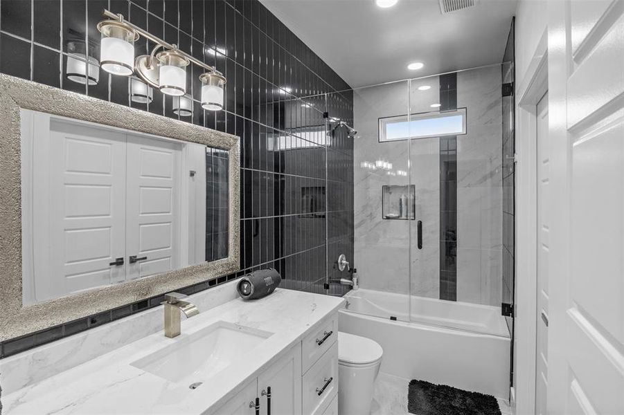 Bathroom with bath / shower combo with glass door, vanity, tile walls, and recessed lighting Bathroom with bath / shower combo with glass door, vanity, tile walls, and recessed lighting