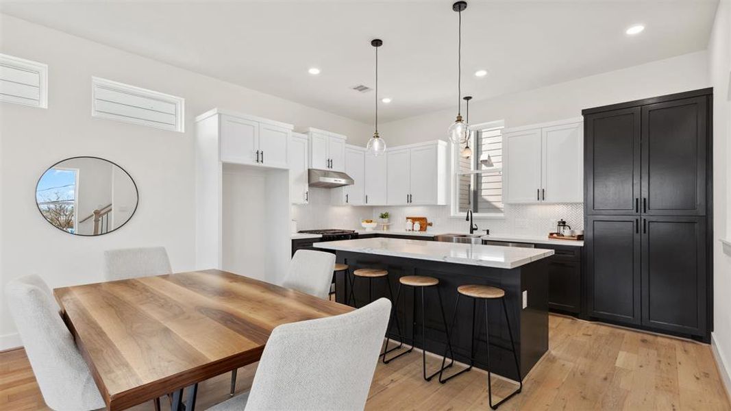 Chefs open kitchen and living space features stainless steel appliances, a modern island with a sink, quartz countertops, and custom black matte pendant lighting.