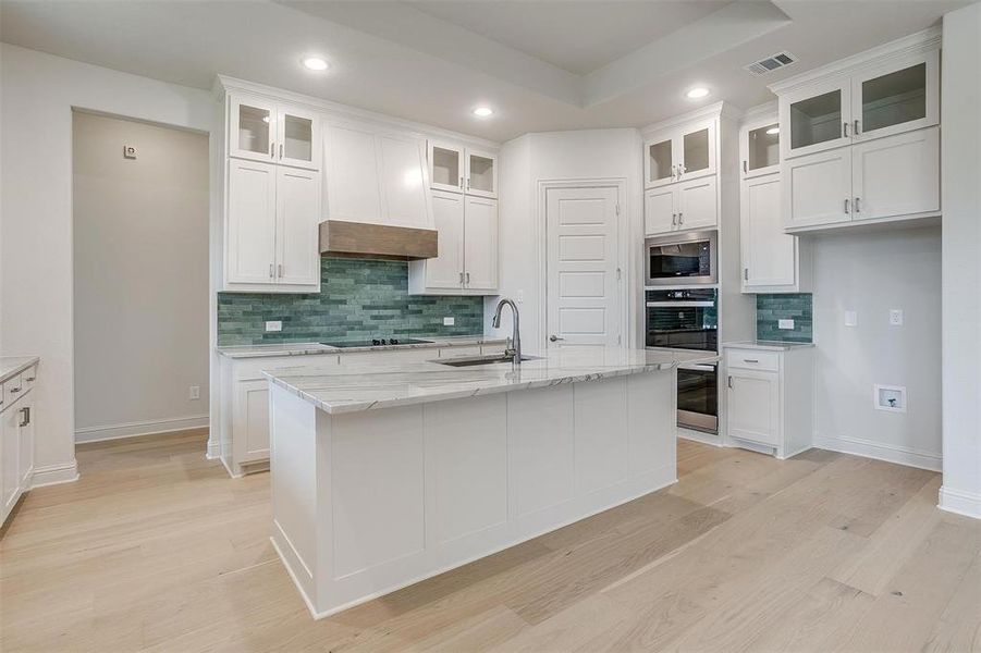 Kitchen featuring tasteful backsplash, white cabinetry, light stone countertops, sink, and an island with sink