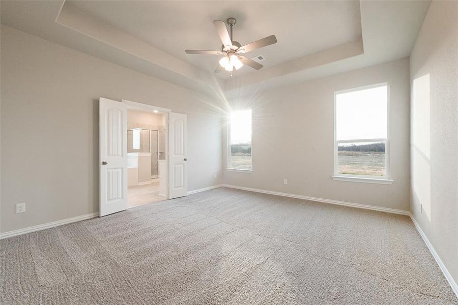 Unfurnished bedroom with light colored carpet, a raised ceiling, ceiling fan, and ensuite bath