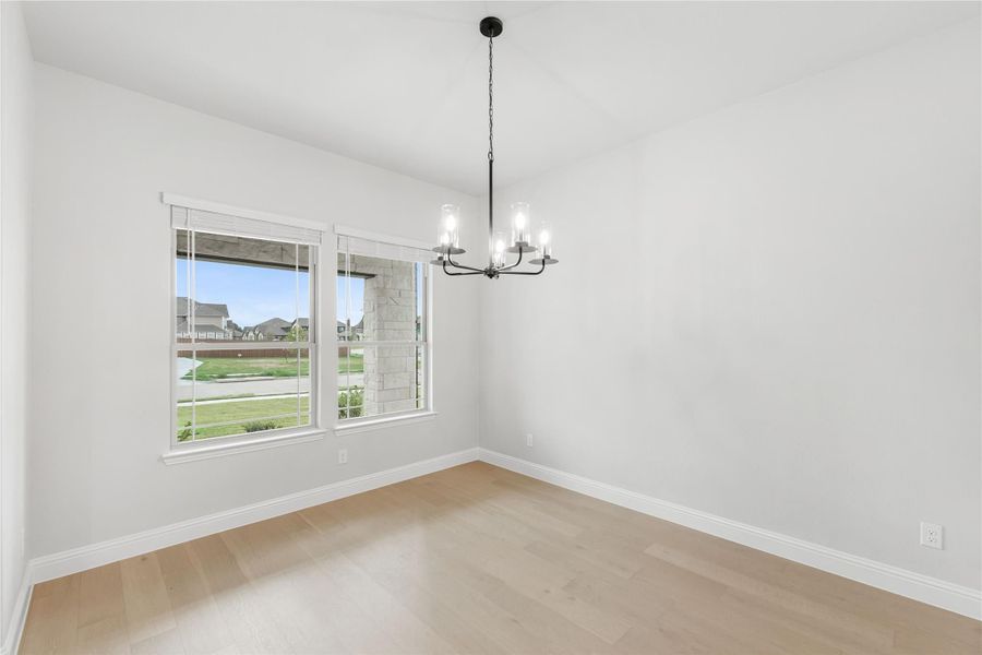 Empty dining room with light wood floors, black chandelier, and two windows with neighborhood view