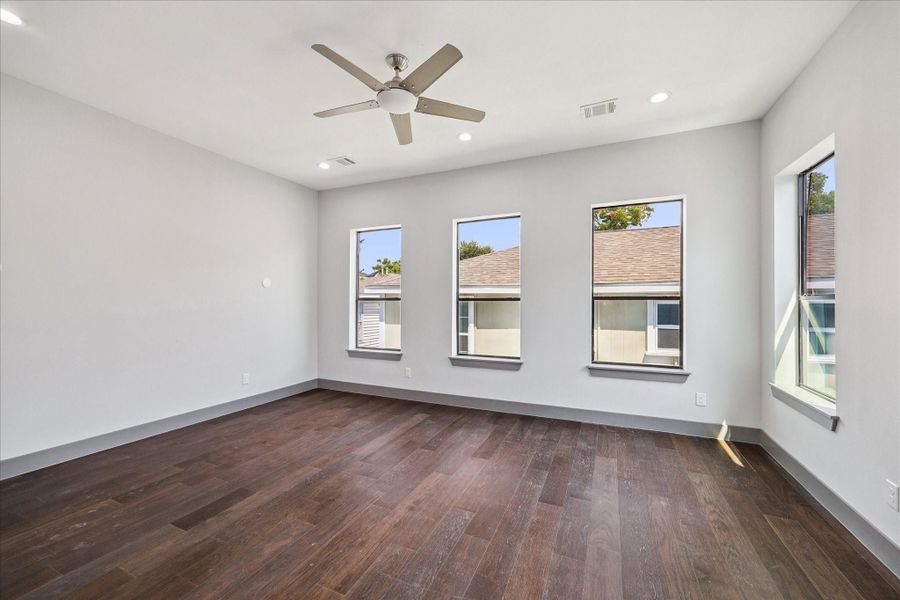 Spacious and inviting, the primary bedroom showcases wood floors, recessed lighting, and large windows that flood the room with natural light, creating a serene retreat.
