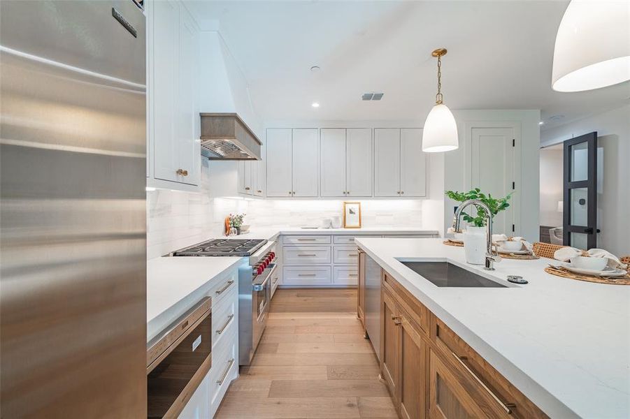 Kitchen with white cabinets, sink, pendant lighting, and high end appliances