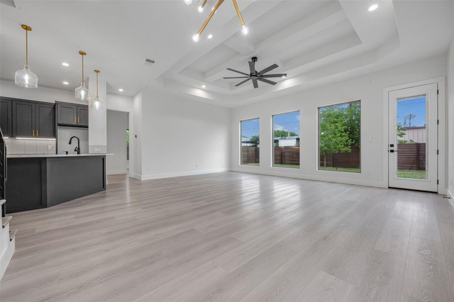 Spacious, unfurnished living room featuring recessed lighting, a ceiling fan, tray ceiling, detailed baseboards, and light wood-finished flooring. Spacious, unfurnished living room featuring recessed lighting, a ceiling fan, tray ceiling, detailed baseboards, and light wood-finished flooring.