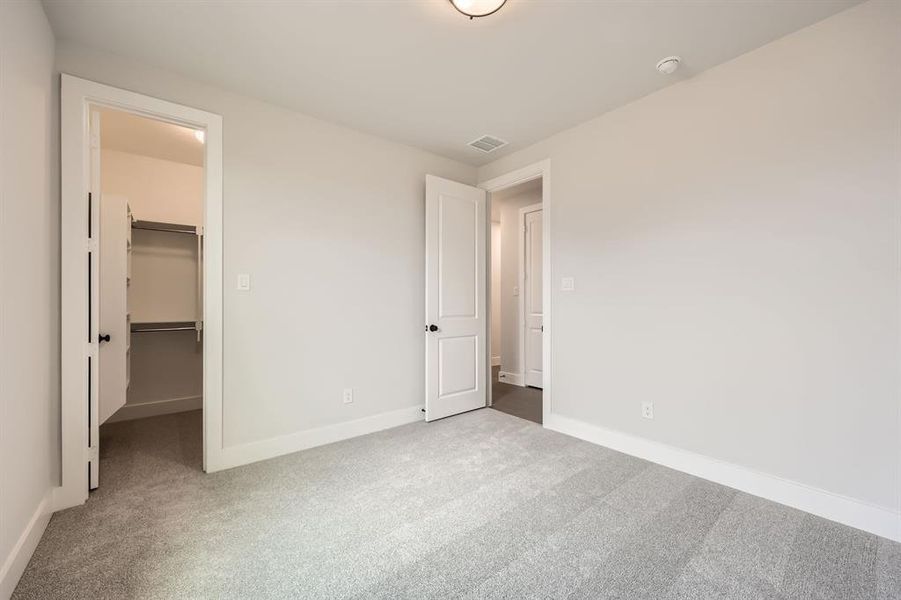 Unfurnished bedroom with a closet, carpet flooring, a walk in closet, baseboards, and visible vents Unfurnished bedroom with a closet, carpet flooring, a walk in closet, baseboards, and visible vents