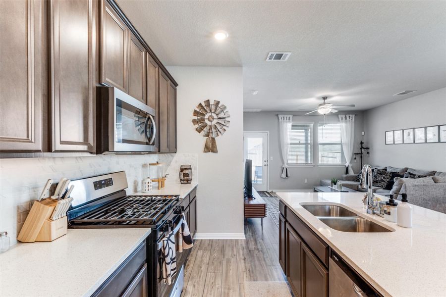 Kitchen featuring stainless steel appliances, open floor plan, light stone counters, light wood finished floors, and dark brown cabinetry
