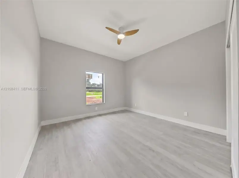 Neutral-toned interior space featuring wood-finish flooring, a contemporary three-blade ceiling fan with integrated lighting, and a single-pane window