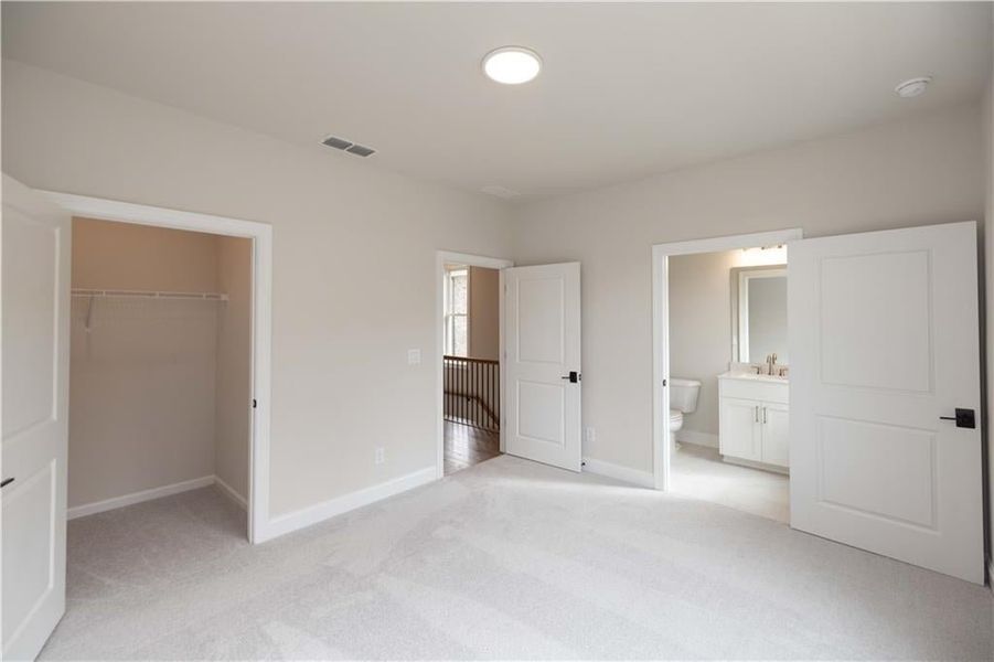 Unfurnished bedroom featuring connected bathroom, sink, a walk in closet, light colored carpet, and a closet