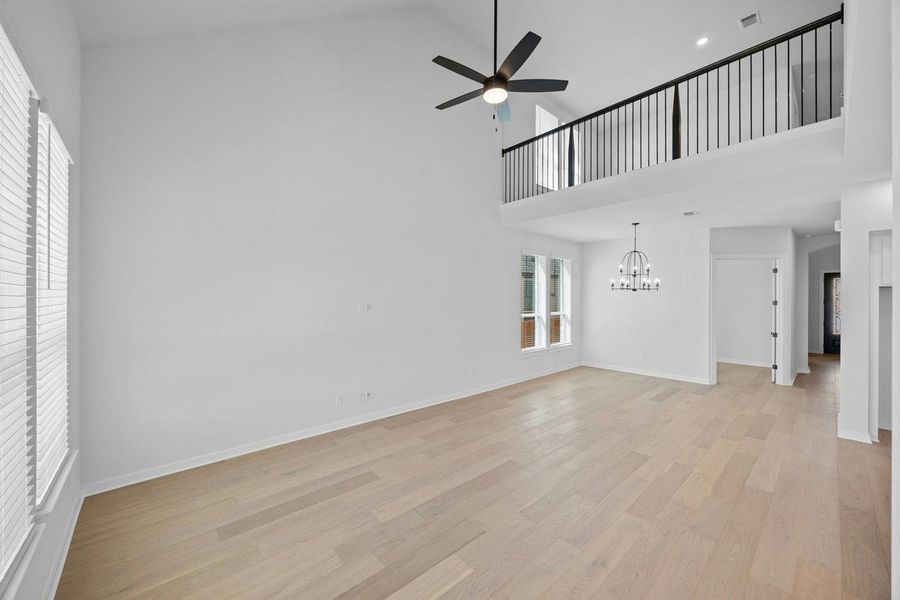 Unfurnished living room featuring a chandelier, ceiling fan, high vaulted ceiling, and light wood-style floors Unfurnished living room featuring a chandelier, ceiling fan, high vaulted ceiling, and light wood-style floors