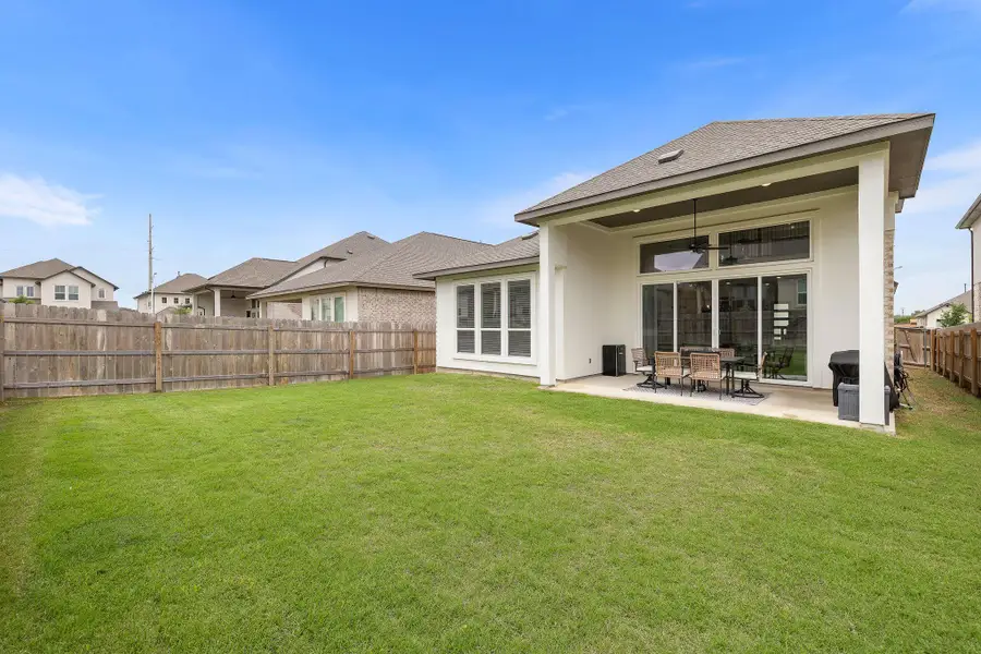 Expansive rear yard featuring a large covered patio with a ceiling fan, concrete slab, and multiple sliding glass doors