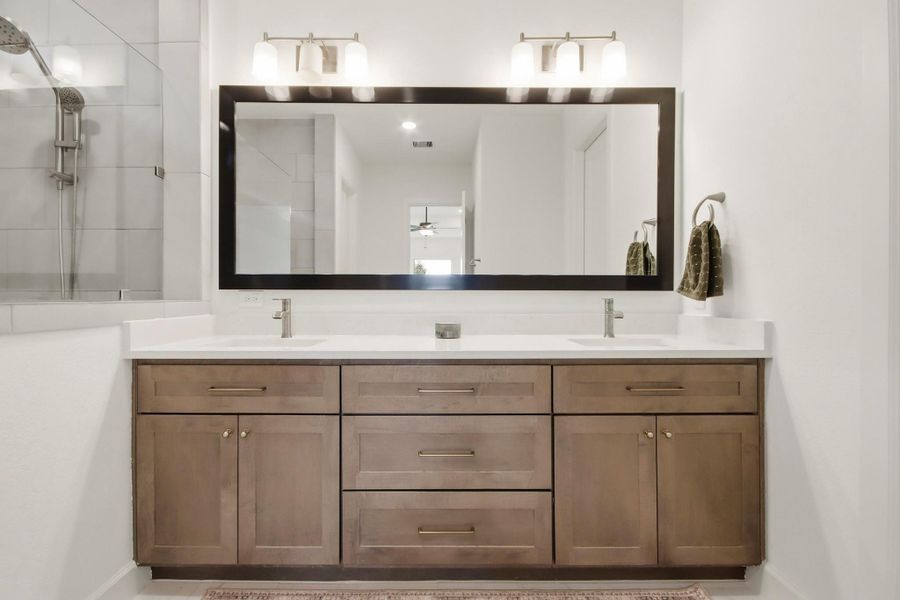 Elegant bathroom featuring a double vanity with sleek sinks, modern lighting, and a spacious mirror, complemented by rich wood cabinetry.