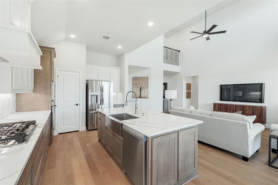 Open-concept kitchen with large island, quartz countertops, and wood floors opening to living room with high ceilings