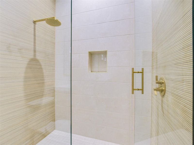 The shower features a rain style shower head and coordinating gold-toned fixtures