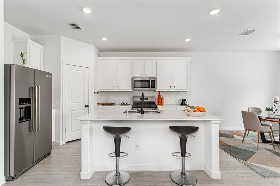 The kitchen features white cabinetry, a white subway tile backsplash, and a large island with a light-colored countertop
