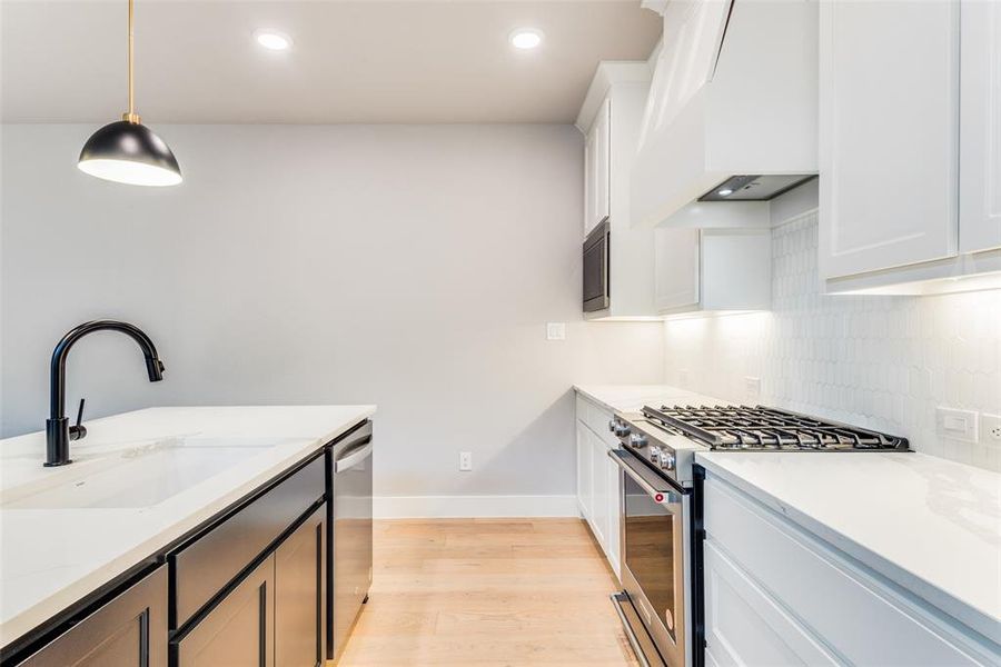 Kitchen featuring white cabinetry, custom range hood, light hardwood / wood-style flooring, stainless steel appliances, and decorative light fixtures