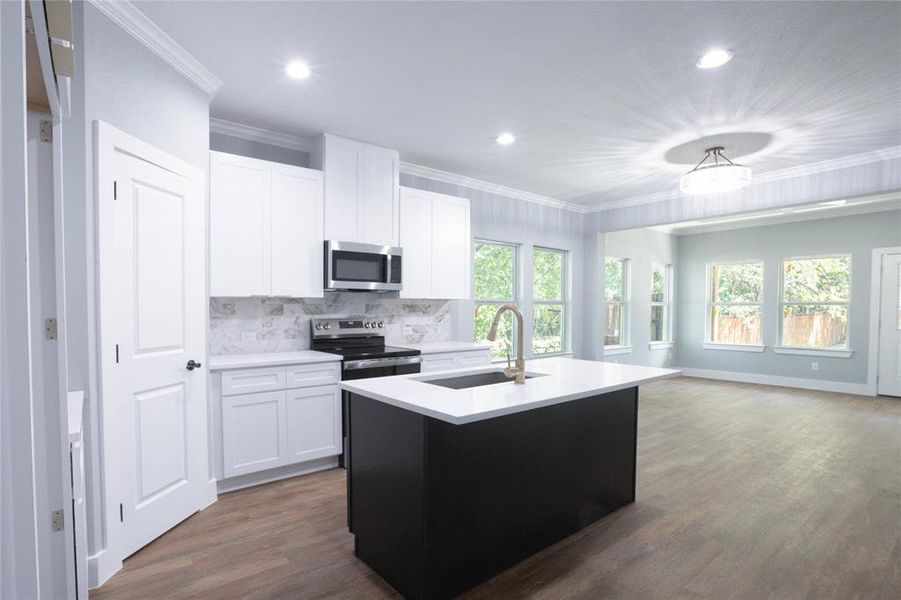Kitchen with backsplash, a kitchen island with sink, white cabinetry, appliances with stainless steel finishes, and ornamental molding