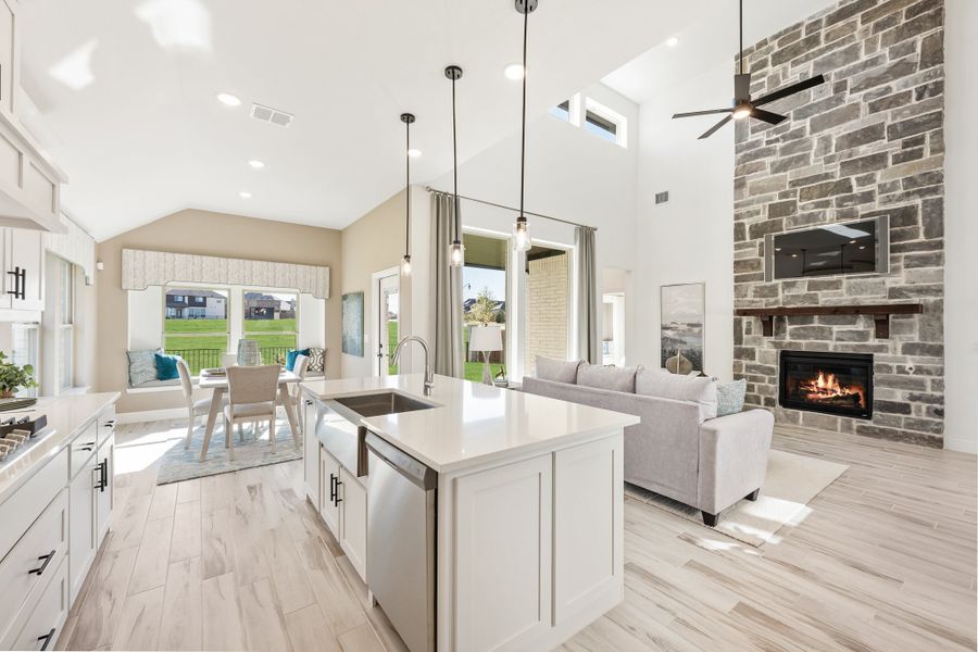Open-concept kitchen and living area with white island, stone fireplace, and vaulted ceiling
