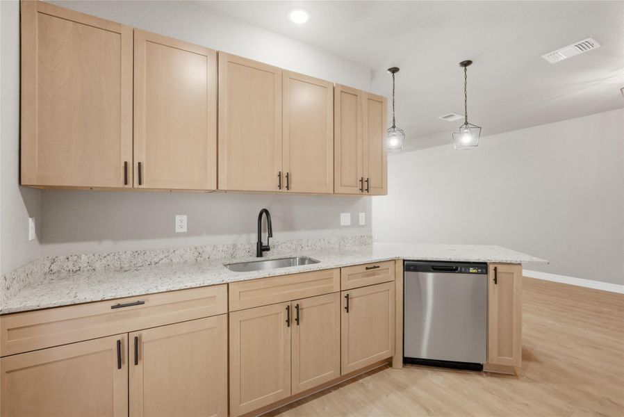 Kitchen with light wood finish cabinets, light stone countertops, stainless steel dishwasher, light wood-style floors, and a peninsula