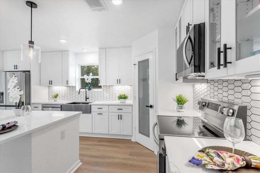 Kitchen featuring stainless steel appliances, light wood floors, white cabinetry, decorative backsplash, and sink