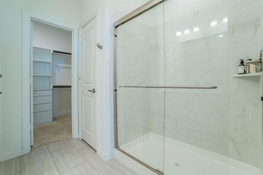 Bathroom featuring a marble finish shower, a spacious closet, light tile patterned flooring, and light carpet Bathroom featuring a marble finish shower, a spacious closet, light tile patterned flooring, and light carpet