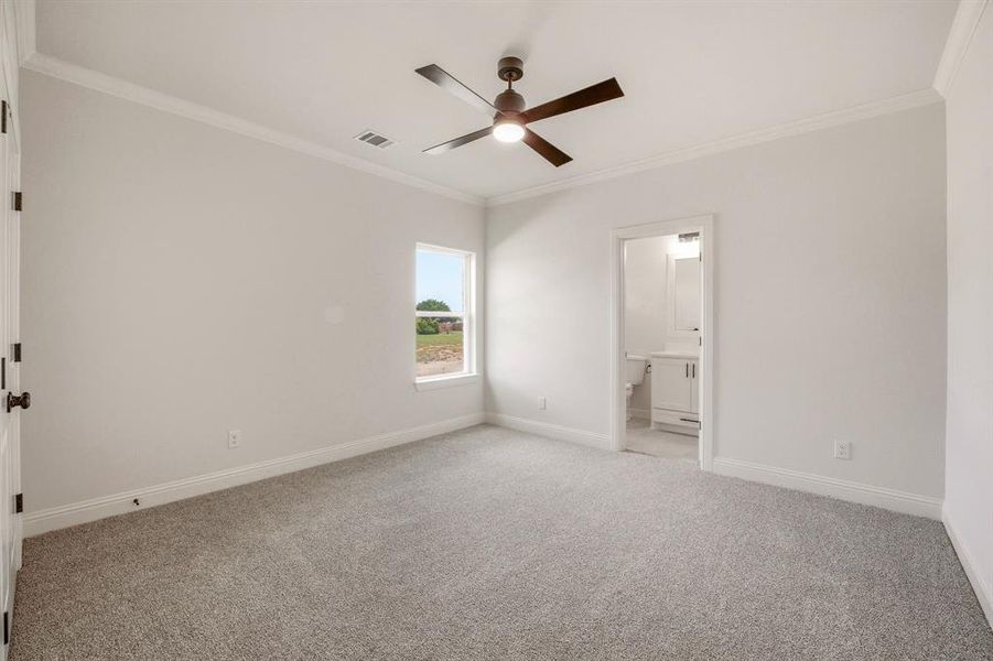 Unfurnished bedroom featuring light colored carpet, ornamental molding, a ceiling fan, and ensuite bath
