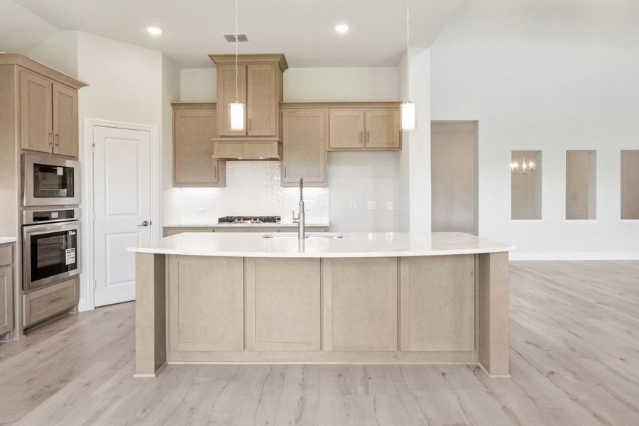 Kitchen with large curved island, light wood cabinets, white countertops, and stainless steel appliances on light hardwood floors