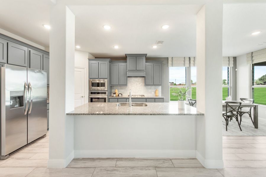 Kitchen with gray cabinets, granite island, stainless steel appliances, and large window overlooking backyard