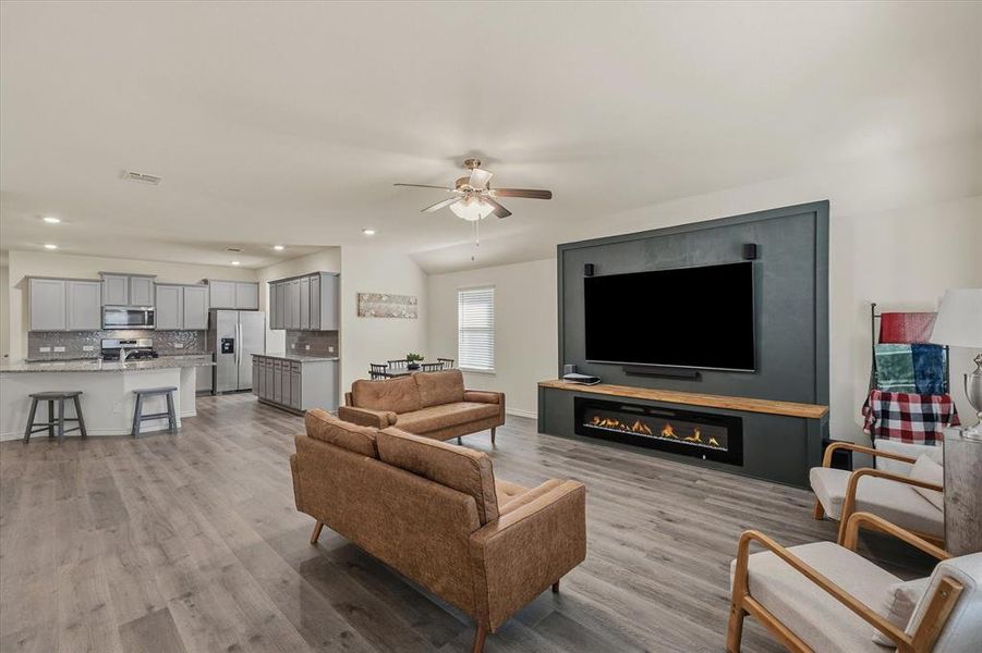 Living room featuring ceiling fan, light wood-type flooring, recessed lighting, vaulted ceiling, and a glass covered fireplace Living room featuring ceiling fan, light wood-type flooring, recessed lighting, vaulted ceiling, and a glass covered fireplace