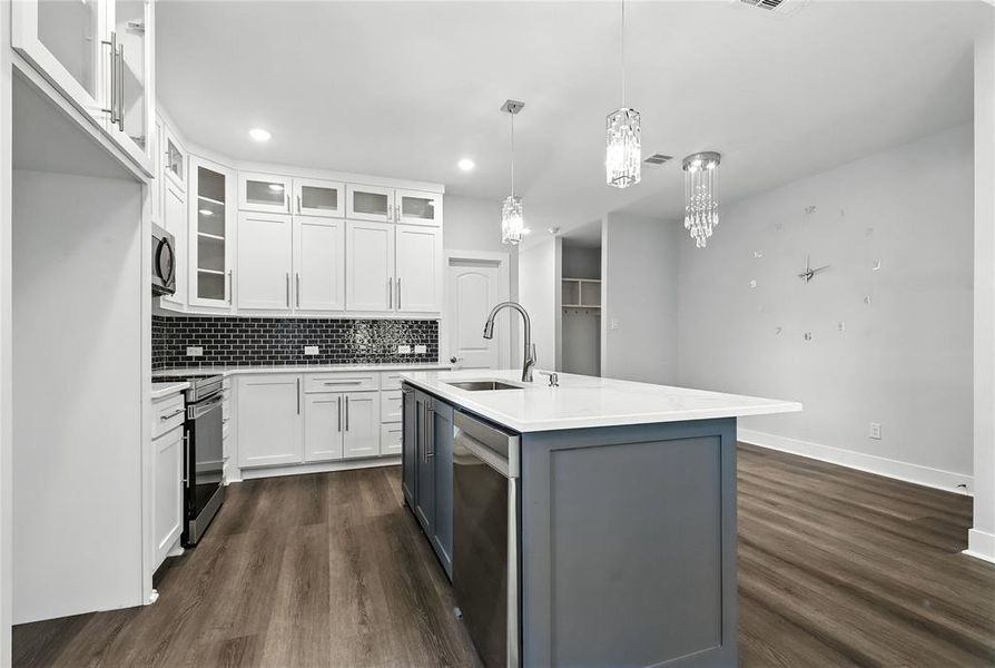 Kitchen featuring dark wood finished floors, white cabinetry, appliances with stainless steel finishes, backsplash, and a kitchen island with sink