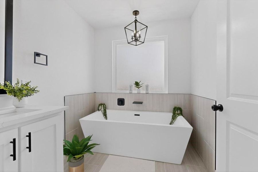 Primary bathroom with vanity, a freestanding tub, a chandelier, and tile walls Primary bathroom with vanity, a freestanding tub, a chandelier, and tile walls