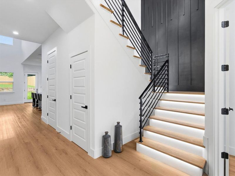 Wood-finish flooring throughout, featuring a staircase with wood treads, integrated step lighting, and iron railings