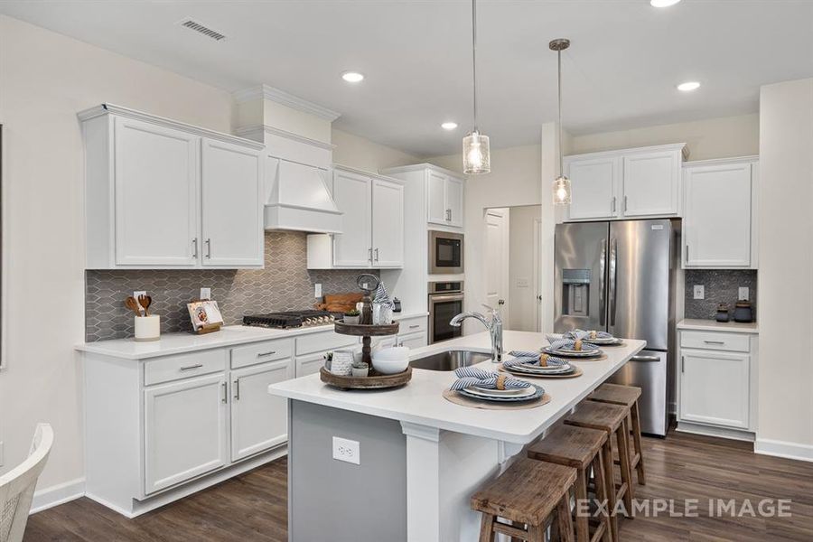 Kitchen featuring decorative backsplash, dark hardwood / wood-style flooring, stainless steel appliances, a kitchen island with sink, and white cabinetry