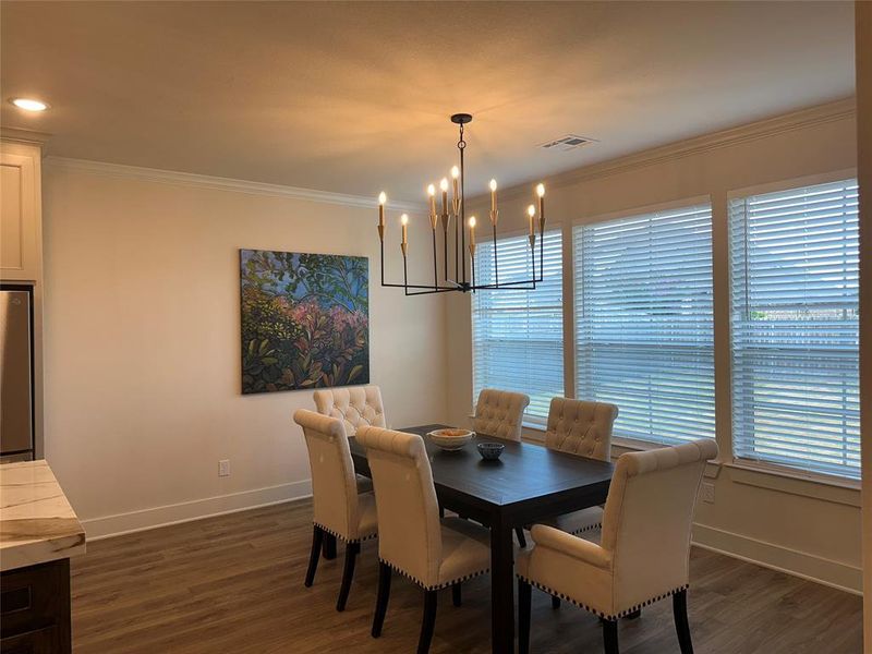 Dining area featuring wood-finish flooring, crown molding, and multiple windows with blinds