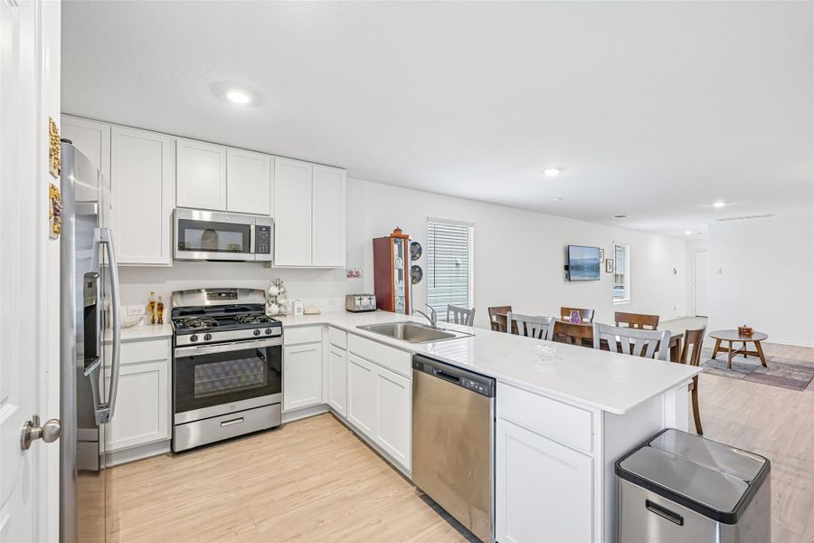 Contemporary kitchen featuring white cabinetry, stainless steel appliances, light-toned wood-finish flooring, white countertops, and recessed lighting Contemporary kitchen featuring white cabinetry, stainless steel appliances, light-toned wood-finish flooring, white countertops, and recessed lighting