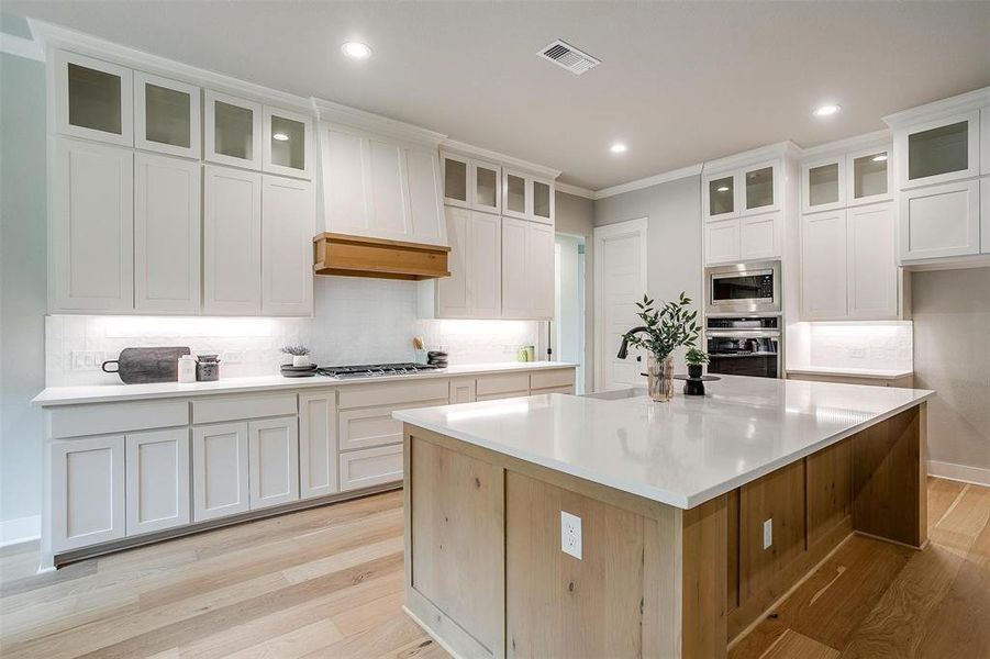 Kitchen featuring stainless steel appliances, a kitchen island with sink, light wood-type flooring, visible vents, and backsplash Kitchen featuring stainless steel appliances, a kitchen island with sink, light wood-type flooring, visible vents, and backsplash