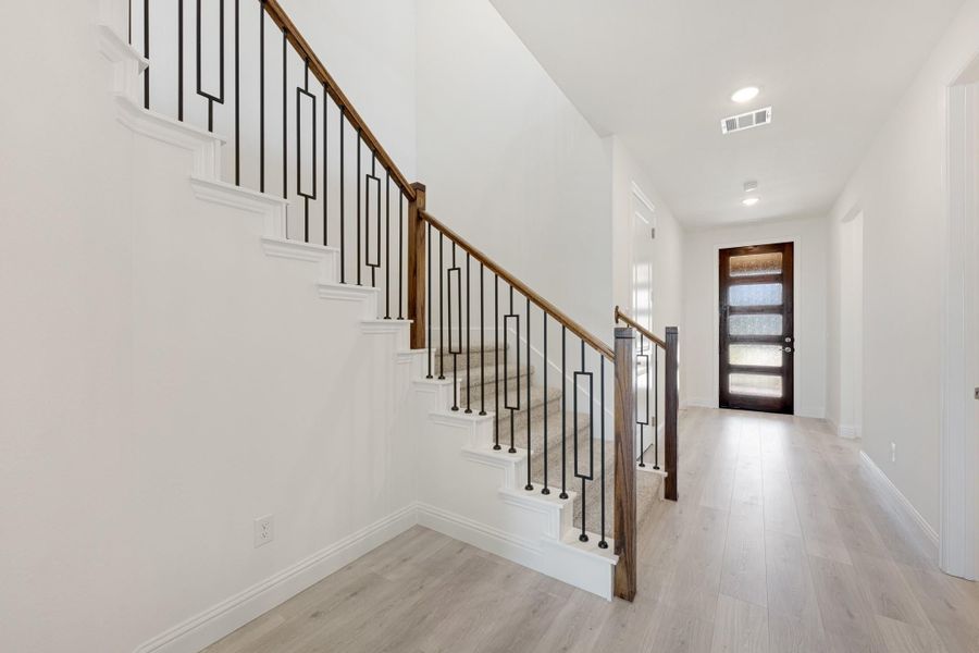 Entryway with carpeted staircase, wood and black iron railing, light hardwood floors, and glass-panel front door Entryway with carpeted staircase, wood and black iron railing, light hardwood floors, and glass-panel front door