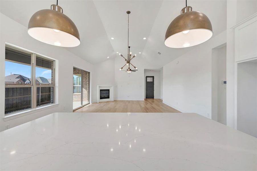 Kitchen with light wood-style floors, open floor plan, a glass covered fireplace, vaulted ceiling, and pendant lighting Kitchen with light wood-style floors, open floor plan, a glass covered fireplace, vaulted ceiling, and pendant lighting