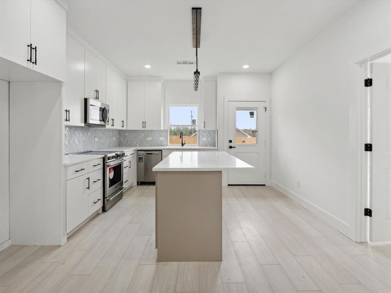 Kitchen featuring stainless steel appliances, a kitchen island, light hardwood / wood-style flooring, white cabinetry, and hanging light fixtures