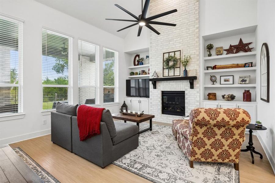 Living area featuring wood-finish flooring, a vaulted ceiling with a ceiling fan, and multiple large windows Living area featuring wood-finish flooring, a vaulted ceiling with a ceiling fan, and multiple large windows