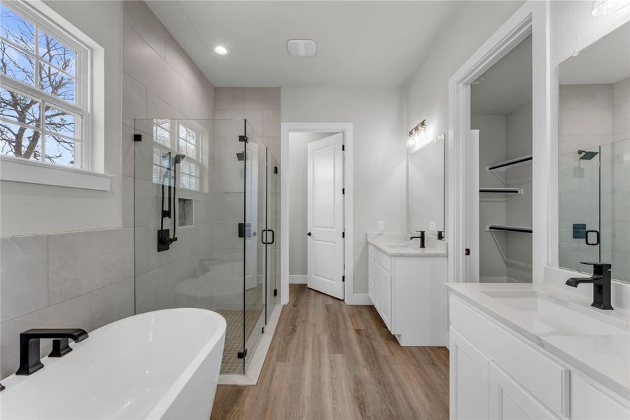Bathroom featuring a stall shower, two vanities, a soaking tub, light wood-style floors, and tile walls