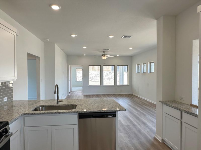 Kitchen featuring white cabinets, light stone countertops, dishwasher, light wood-style flooring, and a peninsula