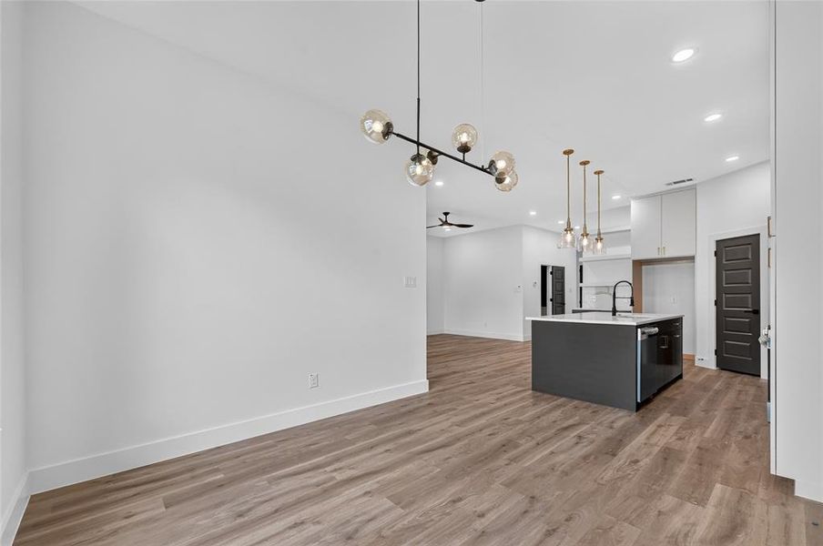 Open-concept interior featuring wood-finish flooring, a modern chandelier, recessed lighting, a kitchen island with sink and integrated dishwasher, and contrasting dark interior doors Open-concept interior featuring wood-finish flooring, a modern chandelier, recessed lighting, a kitchen island with sink and integrated dishwasher, and contrasting dark interior doors