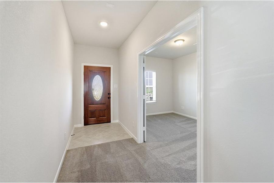 Entryway featuring a rich wood-finish front door with an oval glass insert, recessed lighting, and tile flooring transitioning to soft gray carpeting Entryway featuring a rich wood-finish front door with an oval glass insert, recessed lighting, and tile flooring transitioning to soft gray carpeting