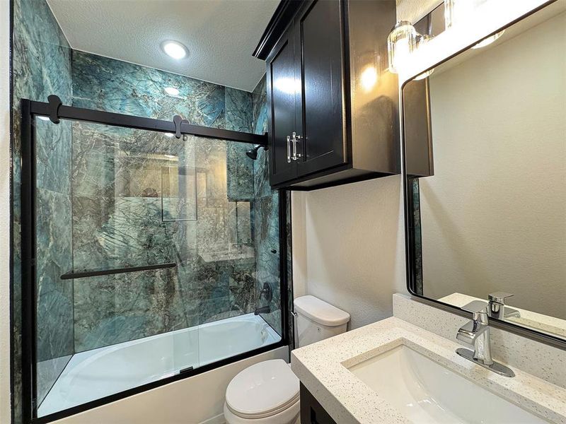 Bathroom featuring a tub/shower combination with a sliding glass enclosure and green-hued stone-look tile surround