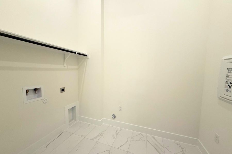 Dedicated laundry area featuring white walls, a white shelf with hanging rod, and white baseboards